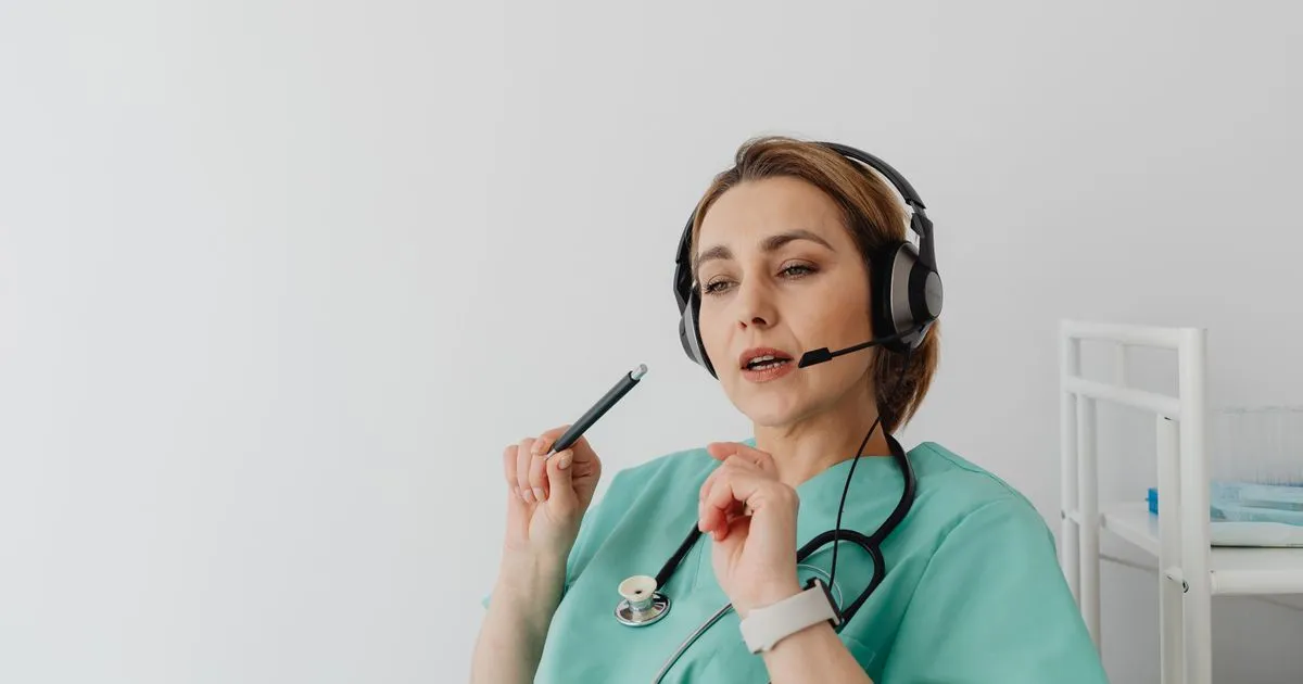 Healthcare worker in scrubs and a headset talks while holding a pen