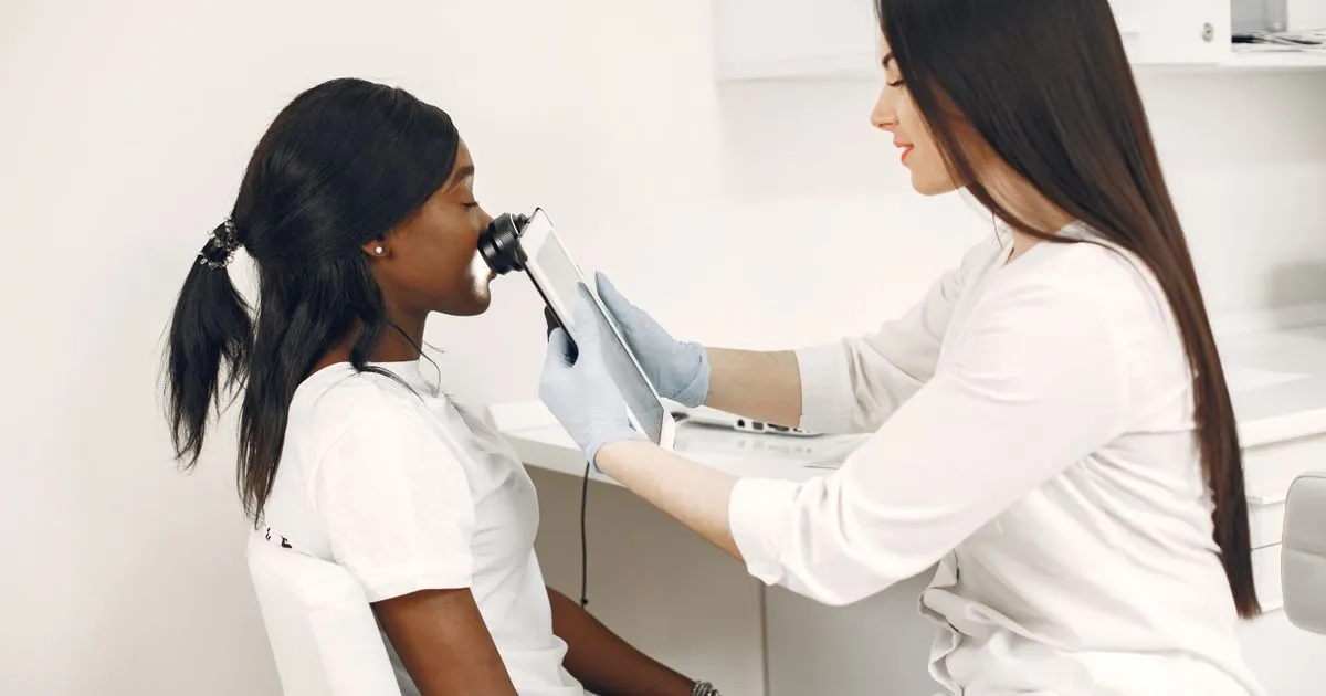 A clinician in gloves examines a seated patient