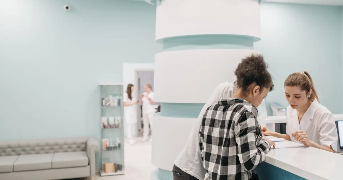 Clinic receptionist reviews paperwork with a patient at a bright front desk.